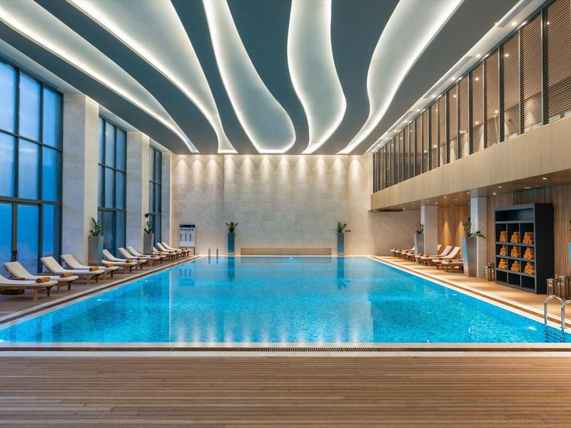 Bright indoor pool with modern wave-shaped lighting and lounge chairs along the edge.
