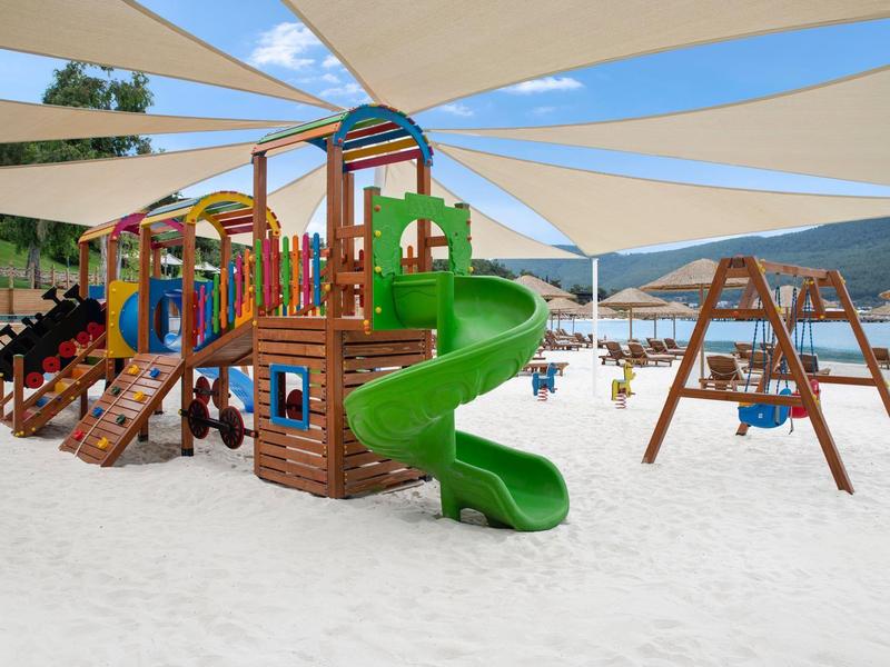 Children's playground with colorful climbing frames and green slide on sandy ground at the beach.
