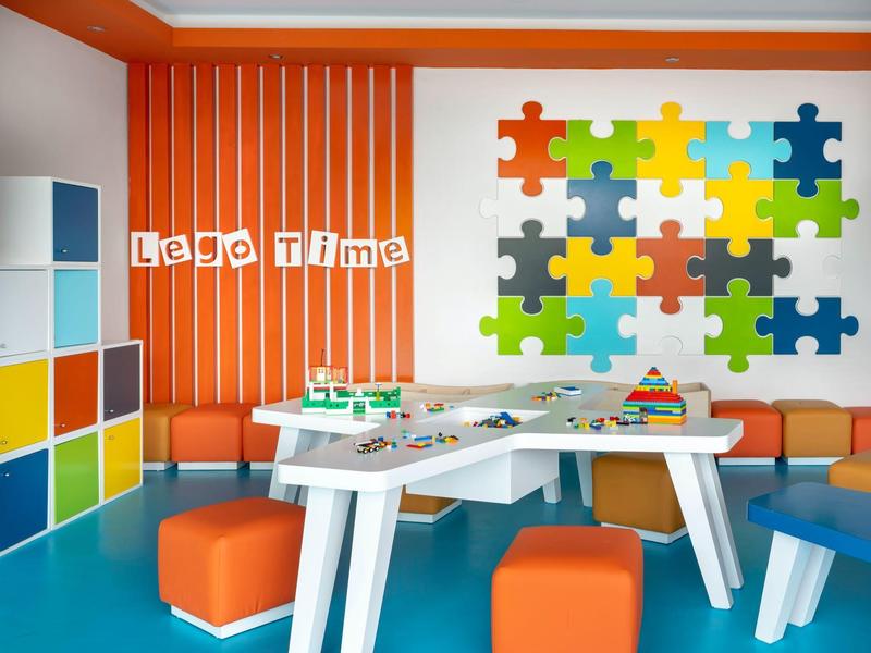 Colorful kids play area with Lego table, orange seats, and puzzle pattern wall.
