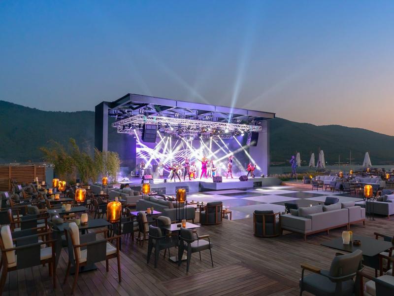 Evening outdoor stage with lighting and seating areas against a mountain backdrop.