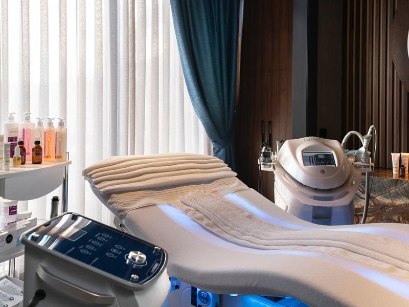 Modern wellness room with relaxing treatment bed and various cosmetic devices.