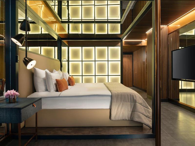 Modern hotel room with large bed, decorative headboard, and indirect lighting.