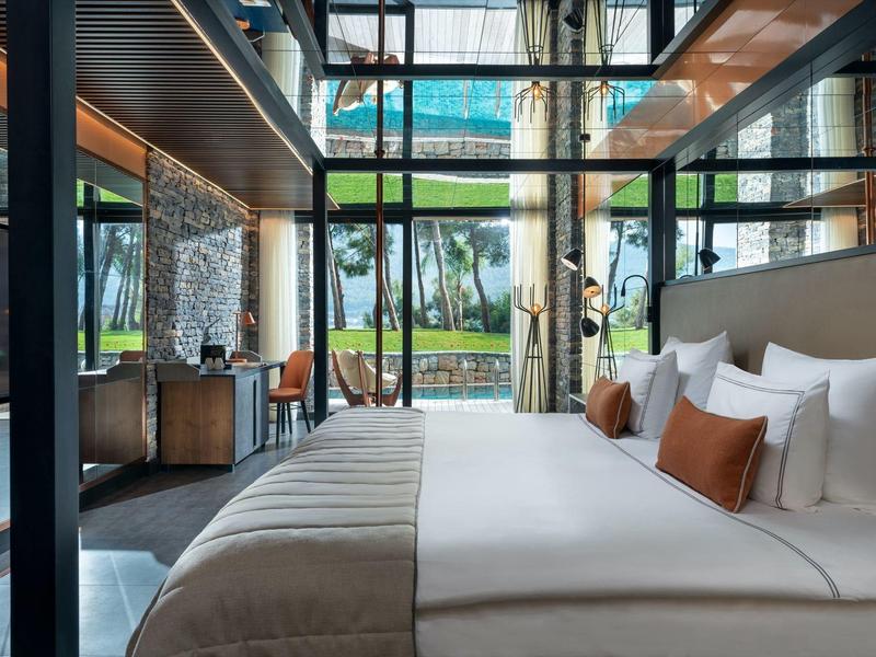 Elegant hotel room with large bed, glass walls, and garden view.
