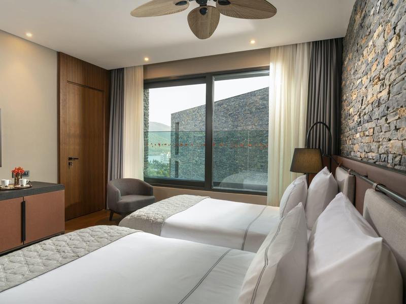 Hotel room with two single beds, large window, and view of forested hill.