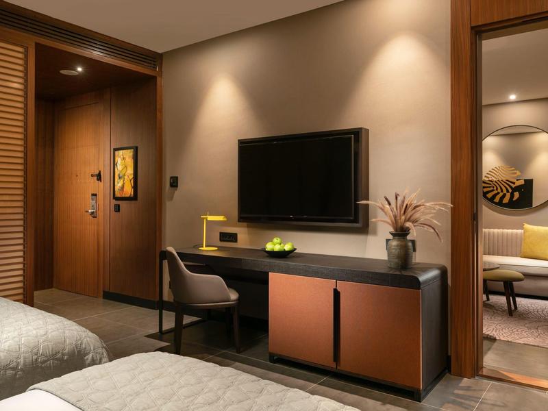 Modern hotel room with TV, desk, and cozy sitting area in the background.