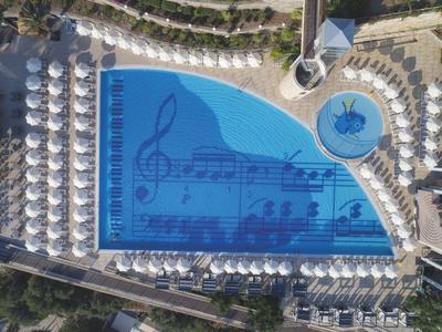 Une piscine d'hôtel unique en forme de piano à queue avec des notes de musique, entourée de parasols blancs.