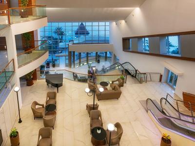 Hall d'hôtel spacieux avec coins salon et escalators sous un éclairage chaud.