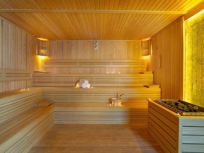 Sauna en bois avec bancs en gradins et un seau en bois avec louche au sol.