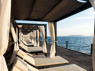 Alignement de lits de plage blancs avec rideaux sur une jetée en bois au bord de la mer au coucher du soleil.
