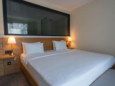 Chambre d'hôtel moderne avec grand lit double, linge blanc, accents en bois et éclairage doux.