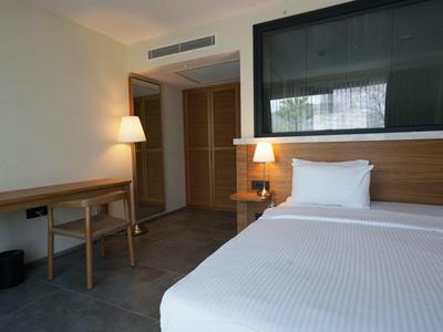 Chambre d'hôtel moderne avec grand lit, bureau en bois, lampe et décoration simple.