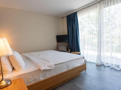 Chambre d'hôtel lumineuse avec grand lit, lampe de chevet et fenêtre du sol au plafond avec rideaux.