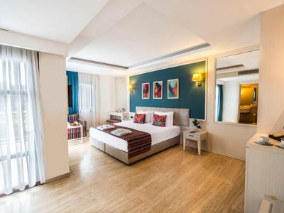 Chambre d'hôtel spacieuse avec grand lit, sol en bois et décoration moderne avec lumière naturelle.