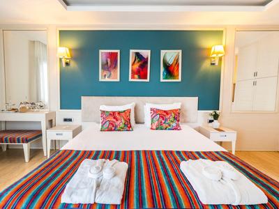 Chambre d'hôtel lumineuse avec lit double, coussins colorés et jeté de lit rayé, tables de chevet et tableaux muraux.