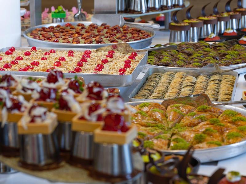 Une variété de desserts incluant gâteaux, pâtisseries et friandises à la pistache disposés sur des plateaux.