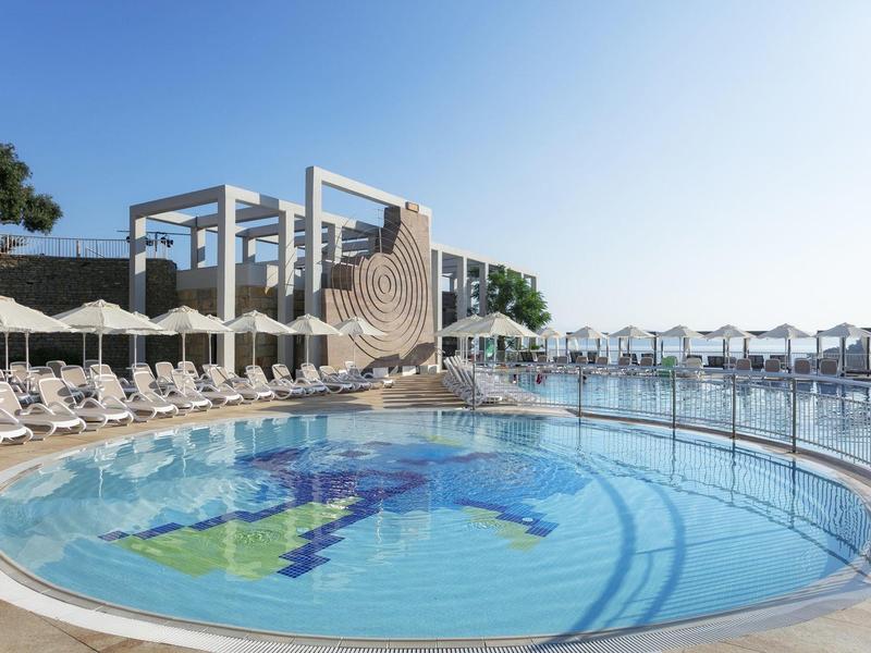 Piscine circulaire extérieure avec chaises longues et structures d'ombre sous un ciel bleu clair