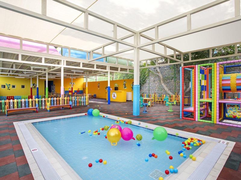 Aire de jeux extérieure colorée pour enfants avec petite piscine et bassin à balles sous toit en verre.