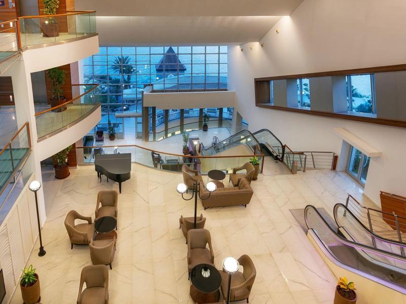 Hall d'hôtel spacieux avec coins salon et escalators sous un éclairage chaud.