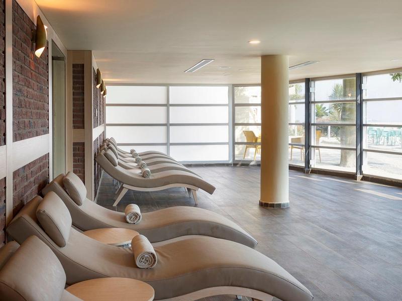 Salon de spa moderne avec chaises courbes, serviettes roulées et grandes fenêtres donnant sur la piscine.