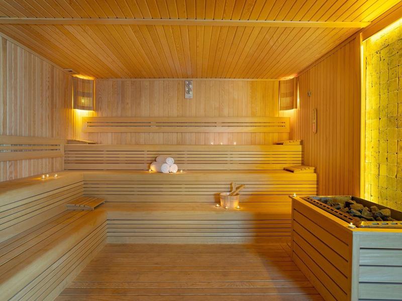 Sauna en bois avec bancs en gradins et un seau en bois avec louche au sol.