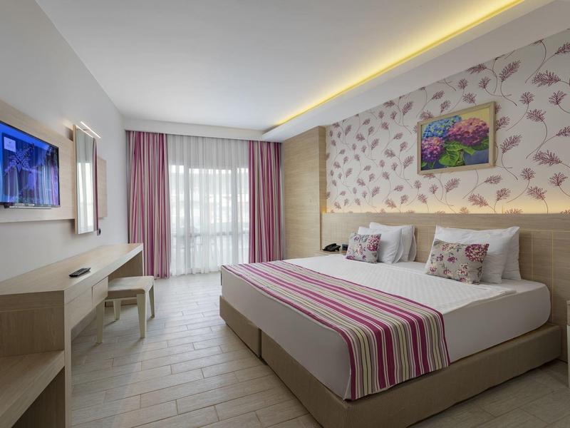 Chambre d'hôtel moderne avec lit double, papier peint floral, bureau et balcon avec rideaux roses.