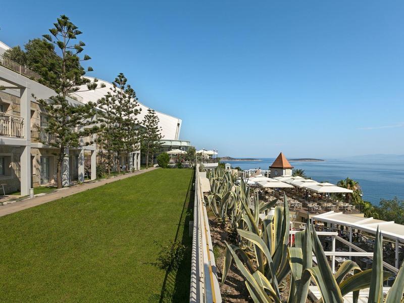 Terrasse d'hôtel surplombant l'océan avec pelouse verte et ciel bleu clair.