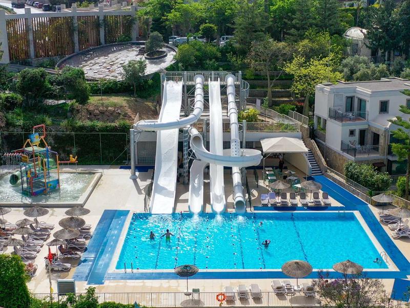 Piscine extérieure d'un complexe avec toboggans aquatiques, chaises longues et verdure.