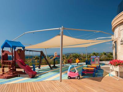 Playground with slide, sandbox, and small play kitchen on a terrace with sea view.