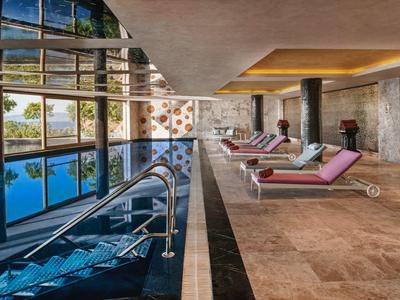 Modern indoor pool with lounge chairs and large glass wall in a hotel.