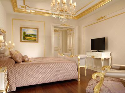 Elegant hotel room with royal bed, chandelier, and gold-trimmed furniture.
