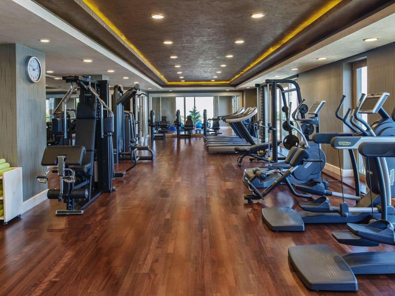 Modern gym with wooden floor, treadmills, ellipticals, and strength machines.