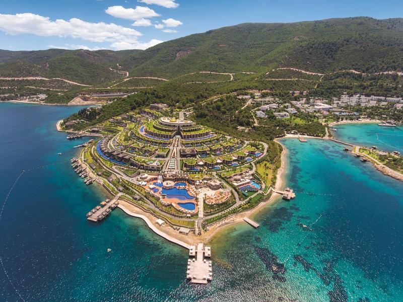 Aerial view of a hotel complex on a peninsula with pools, beaches, and surrounding turquoise sea.