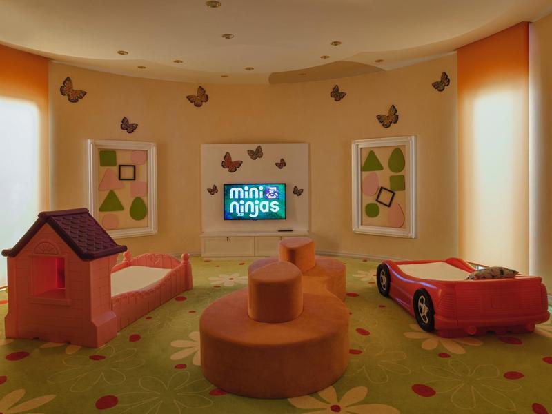 Children's playroom with two beds, a small house, and a car on carpeted floor.