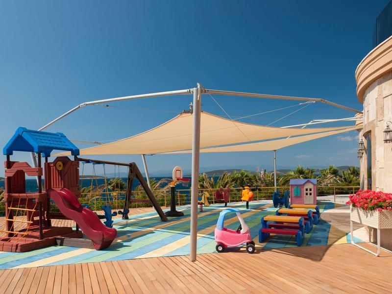 Playground with slide, sandbox, and small play kitchen on a terrace with sea view.