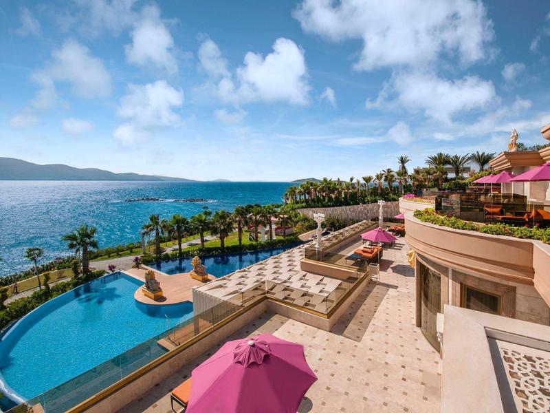 Luxury hotel pool with umbrellas and sea view under clear sky.