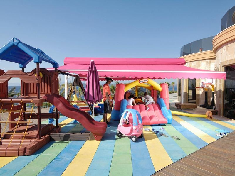 Colorful children's playground with climbing frame, slide, and bouncy castle outside a hotel.