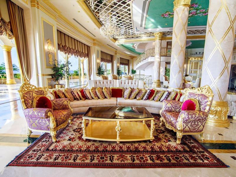 Luxurious hotel lounge with gold-accented columns, elegant furniture, and large decorative rug.