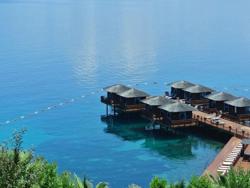 Bungalows on stilts over clear blue water with wooden walkway and green vegetation.