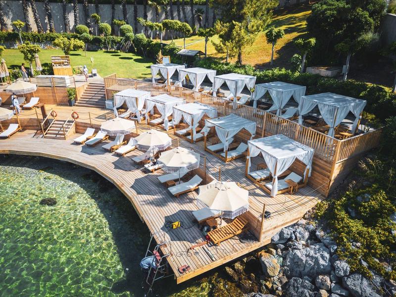 Luxurious terrace with sun loungers and canopy beds by clear water in a green setting