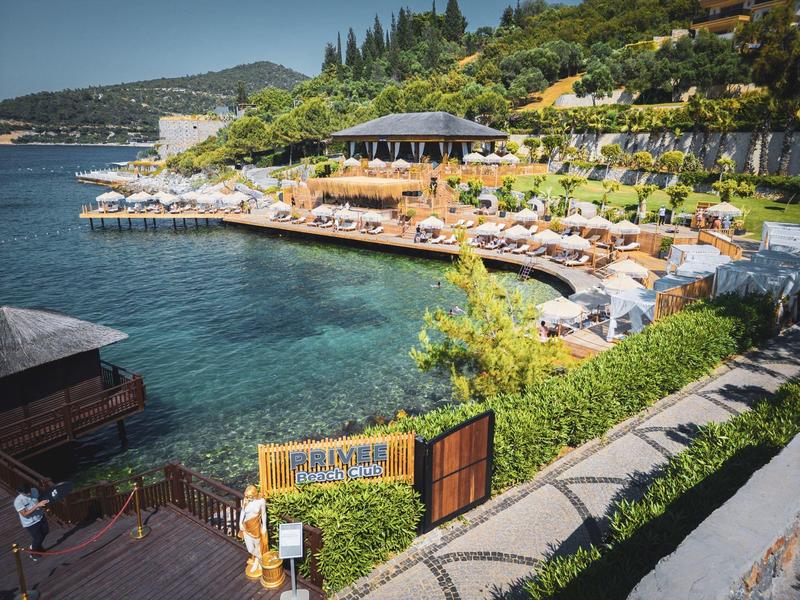 Coastal resort with lounge area, umbrellas, and sunbeds by clear water.