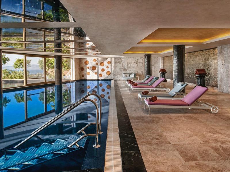 Modern indoor pool with lounge chairs and large glass wall in a hotel.