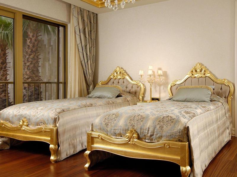 Elegant hotel room with two gold-trimmed single beds and wooden floor