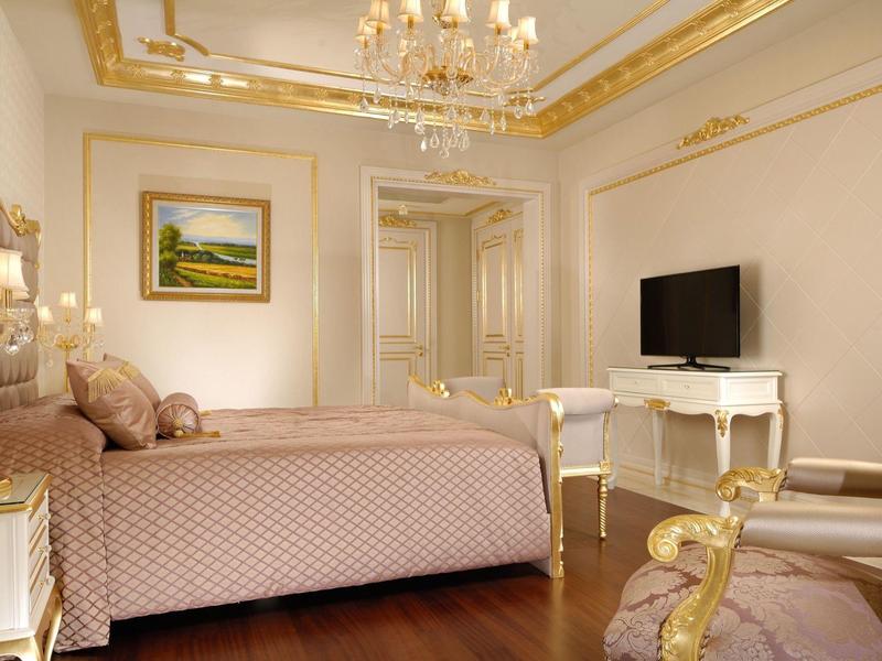 Elegant hotel room with royal bed, chandelier, and gold-trimmed furniture.