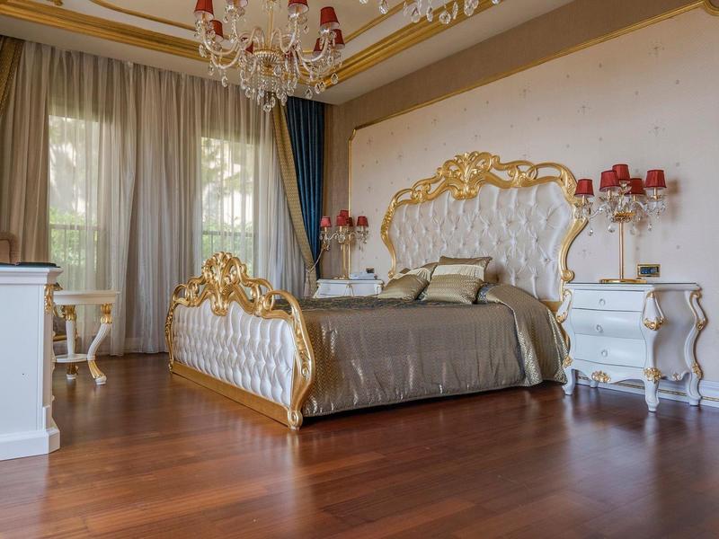 Luxurious hotel room with gilded bed, chandelier, and wooden floor.