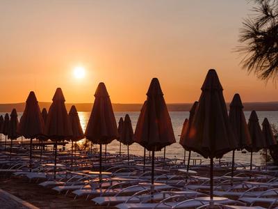 Sonnenuntergang am Strand mit geschlossenen Sonnenschirmen und Schatten der Palmen.