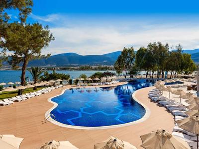 Grande piscina dell'hotel con lettini e ombrelloni accanto a un lago in una giornata di sole.