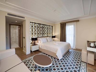 Nowoczesny pokój hotelowy z podwójnym łóżkiem, wzorzystym dywanem i prostymi meblami.