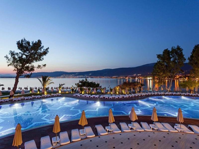 Oświetlony basen o zmierzchu z leżakami i widokiem na morze i wzgórza.