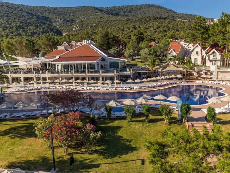Hotel z basenem otoczonym leżakami i zielenią pod niebieskim niebem.