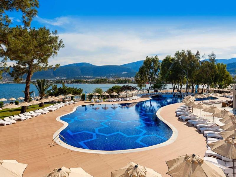 Basen o nieregularnym kształcie z białymi leżakami z widokiem na jezioro i wzgórza.